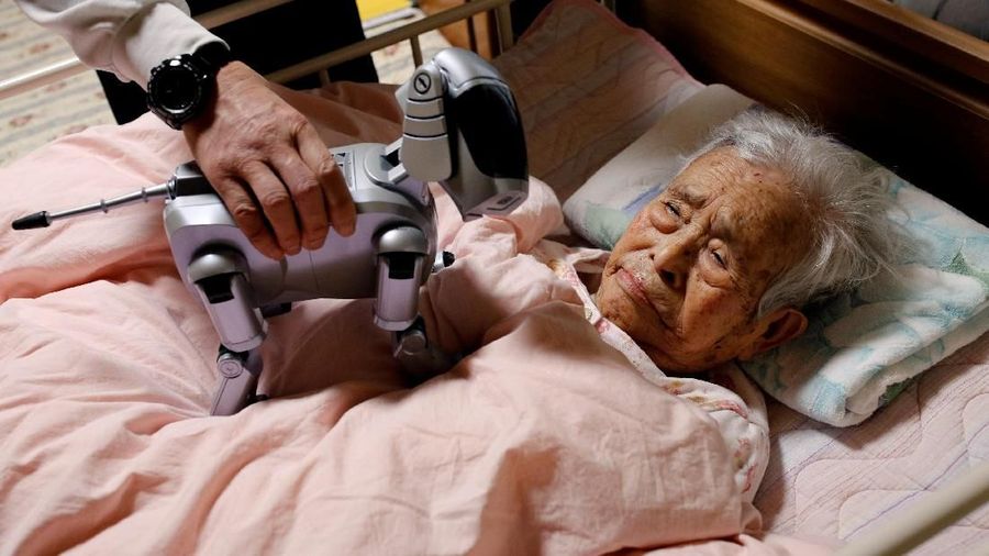 Yoichi Suzuki menunjukkan 'AIBO', robot anjing peliharaan, kepada ibunya yang tinggal di tempat tidur di rumahnya di Takahagi, Prefektur Ibaraki, Jepang, 6 Februari 2018. Ayah Yoichi Suzuki menggunakan 'AIBO' untuk rehabilitasi. REUTERS / Kim Kyung-Hoon
