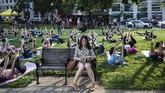 Seorang perempuan duduk di bangku dan asik membaca sementara di sekelilingnya orang-orang sedang mengikuti kelas Yoga di sebuah taman di Washington DC, Amerika Serikat. (AFP PHOTO / Andrew CABALLERO-REYNOLDS)