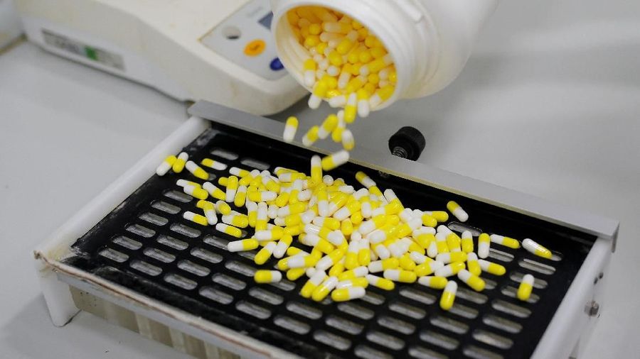 A laboratory technician places medication capsules on a capsules counter during packaging in a laboratory at 