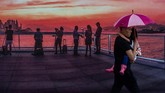 Seorang pria yang membawa payung menggendong anaknya berjalan melewati sebuah poster yang menggambarkan matahari termbenam di Hong Kong. (AFP PHOTO / Philip FONG)