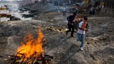 Sejumlah orang India berlari melewati tumpukan kayu bakar di Varanasi. Asap dan abu dari jenazah yang dibakar memenuhi udara kawasan itu. (AFP PHOTO / CHANDAN KHANNA)