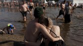 Sepasang pengunjung melihat pengunjung lainnya bermain lumpur. Para wanita tak jarang mengenakan bikini atau bahkan menanggalkan bajunya di festival ini. (REUTERS/Kacper Pempel)