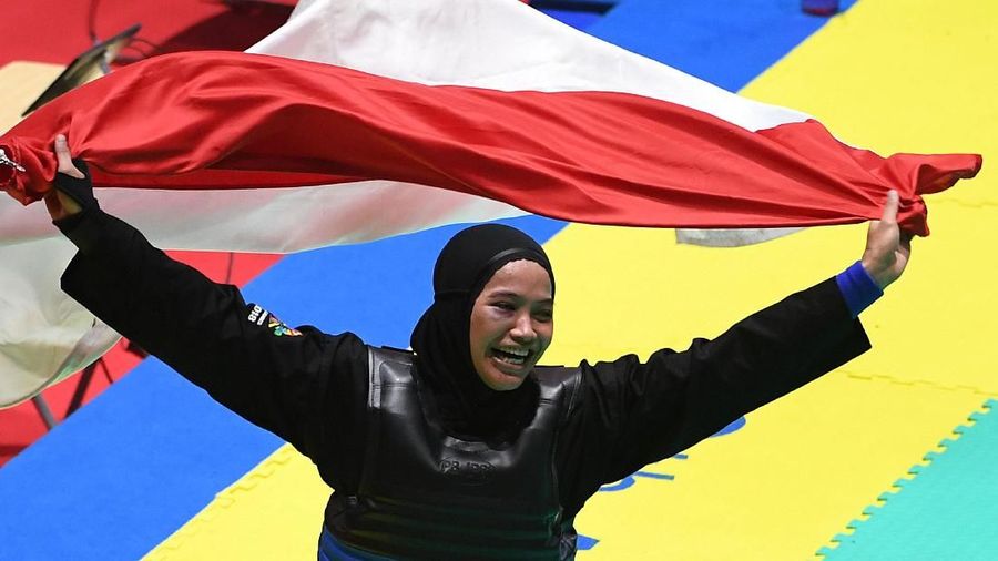 Pesilat Indonesia Sarah Tria Monita membentangkan bendera merah putih usai mengalahkan pesilat Laos Nong Oy Vongphakdy (kiri) dalam babak final Kelas C Putri Asian Games 2018 di Padepokan Pencak Silat Taman Mini Indonesia Indah (TMII), Jakarta, Senin (27/8). ANTARA FOTO/INASGOC/Melvinas Priananda/nak/18.