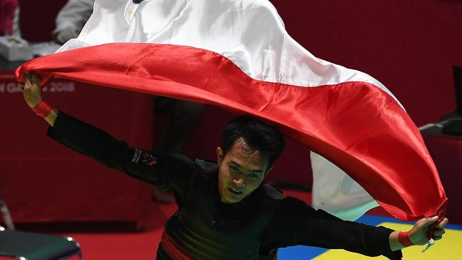 Pesilat Indonesia Komang Harik Adi Putra berlari membentangkan bendera merah putih usai mengalahkan pesilat Malaysia Mohd Al Jufferi Jamari dalam babak final Kelas E Putra Asian Games 2018 di Padepokan Pencak Silat Taman Mini Indonesia Indah (TMII), Jakarta, Senin (27/8). ANTARA FOTO/INASGOC/Melvinas Priananda/nak/18.