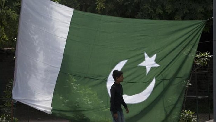 PAKISTAN/ A boy walks past a Pakistani flag displayed for sale ahead of Pakistan's Independence Day, along a road in Rawalpindi August 12, 2012. Pakistan commemorates its Independence Day on August 14. REUTERS/Faisal Mahmood (PAKISTAN - Tags: SOCIETY ANNIVERSARY POLITICS) - RTR36QOE