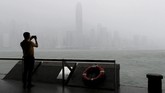 Seorang pria mengambil foto saat hujan lebat turun di Pelabuhan Victoria pada Minggu (16/9). (REUTRERS/Bobby Yip)
