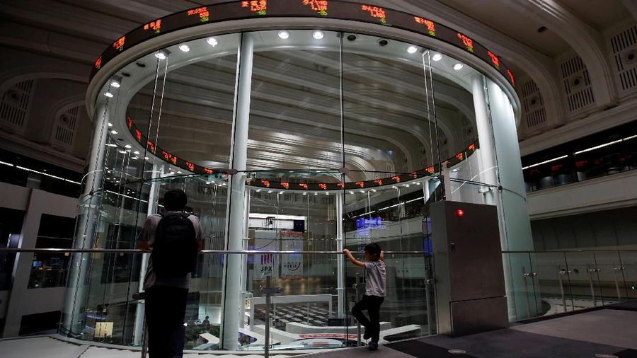 A passerby walks past an electronic board displaying a graph showing recent movement of Japan's Nikkei average outside a brokerage in Tokyo, Japan, October 11, 2018. REUTERS/Issei Kato