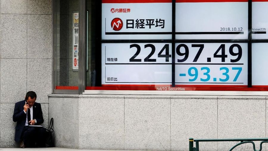 A man uses a mobile phone next to an electronic board showing Japan's Nikkei average outside a brokerage in Tokyo, Japan, October 12, 2018.   REUTERS/Toru Hanai