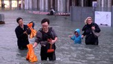 Para turis dan warga setempat terpaksa menerjang genangan air setinggi pinggang untuk beraktivitas. (Reuters/Manuel Silvestri)