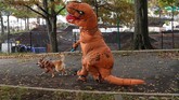 Seekor anjing berjalan dengan tuannya yang berkostum dinosaurus pada parade Annual Tompkins Square Halloween Dog Parade ke-28 di East River Park Amphitheatre, New York. (AFP/Timothy A. Clarly)