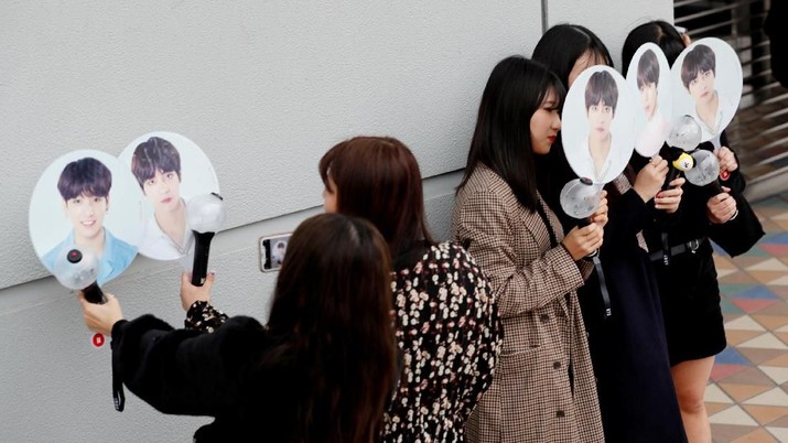 Pengunjung konser berfoto dengan penggemar yang membawa foto anggota boy band Korea Selatan di luar Tokyo Dome saat konser band akan diadakan di Tokyo, Jepang, 13 November 2018. REUTERS / Kim Kyung-Hoon People take their photos with fans bearing photos of the members of South Korean boy band BTS outside Tokyo Dome where the band's concert will be held in Tokyo, Japan, November 13, 2018. REUTERS/Kim Kyung-Hoon