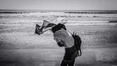Momen merupakan bagian dari aspek fotografi jalanan. Kesigapan merekam obyek foto memang diperlukan ditambah penguasaan kamera yang digunakan. Pande Parwata berhasil merekam momen fotografi jalanan dari seorang pengunjung yang mencoba mempertahankan payungnya dari terpaan angin pantai.
