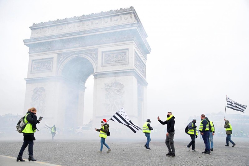 Protesters wearing yellow vest, a symbol of a French drivers' protest against higher fuel prices, stand up in front of a police water canon during clashes on the Champs-Elysees in Paris, France, November 24, 2018. REUTERS/Benoit Tessier