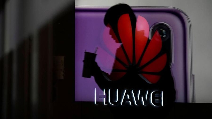A man walking past a Huawei P20 smartphone advertisement is reflected in a glass door in front of a Huawei logo, at a shopping mall in Shanghai, China December 6, 2018. REUTERS/Aly Song