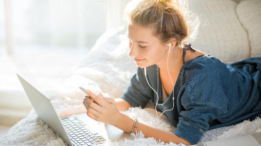 Portrait of an attractive woman lying on the bed with laptop and phone, white soft bed cover, concept photo