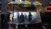 Para pedagang makanan jalanan berteduh ketika hujan datang di kota Manhattan, New York, Amerika Serikat. (REUTERS/Amr Alfiky)