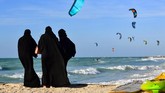 Para perempuan yang mengenakan hijab dan cadar berdiri di suatu pantai di Dubaui sambil menyaksikan layang-layang. (Photo by GIUSEPPE CACACE / AFP)
