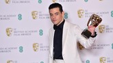 Rami Malek memilih kombinasi hitam dan putih dari kemeja dan single breasted tuxedo dari Berluti. (Photo by Ben STANSALL / AFP)