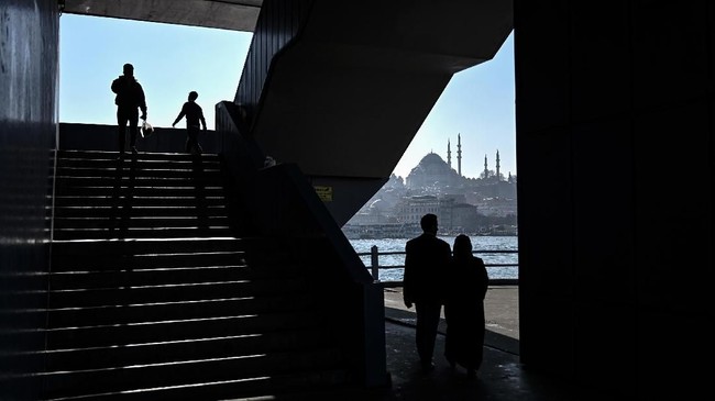 Pada suatu hari yang cerah, orang-orang berjalan di jembatan Galata di depan masjid Suleymaniye di distrik Karakoy di Istanbul. (Photo by OZAN KOSE / AFP)