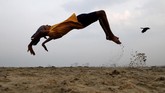 Seorang bocah laki-laki berlatih salto sembari berolahraga di suatu pantai di Kochi, India. (REUTERS/Sivaram V)