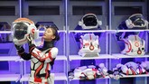 Seorang anggota staf mendemonstrasikan bagaimana dia mengenakan helm dan setelan baju tiruan untuk hidup di Mars. (REUTERS/Thomas Peter)