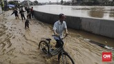 Warga melintasi genangan di kawasan Jatinegara Jakarta Timur, Jumat (26/4). Luapan kali Ciliwung membuat sejumlah jalan tergenang air. Kali meluap setelah hujan mengguyur wilayah Bogor dan menyebabkan debit air naik. (CNN Indonesia/Adhi Wicaksono)