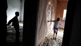 Seorang bocah bermain bola di dekat mural yang dilukis oleh seniman Palestina, Ali Al-Jabali. Mural itu terletak pada suatu bangunan di Gaza yang separuhnya hancur akibat perang antara tentara Israel dan Hamas. (AP Photo/Hatem Moussa)