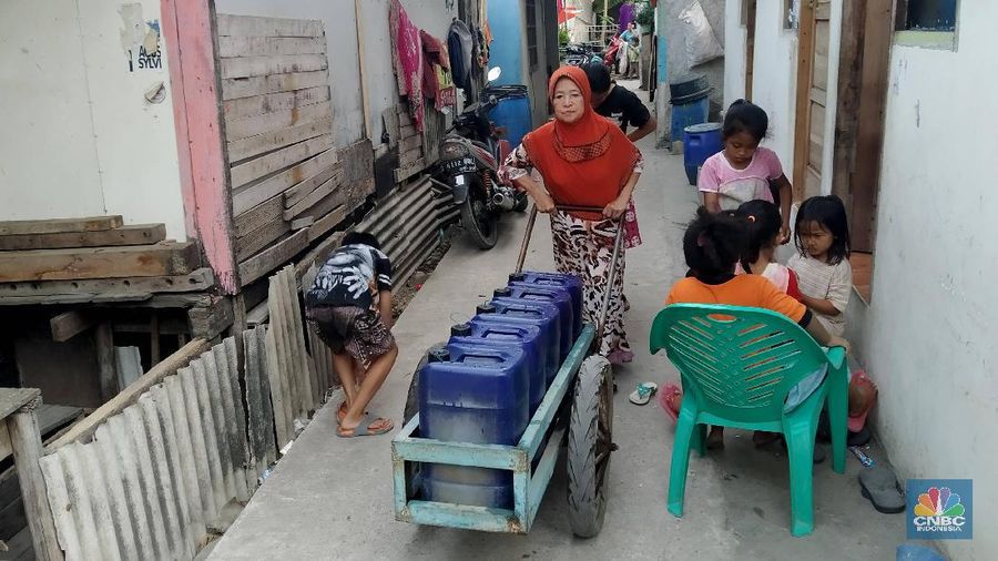 warga memperbaiki posisi pipa yang terpasang menyambung di talang tepi atap rumahnya dan menjulur ke bawah menempel pada tong air berwarna biru tua di kampung Kamal Muara Jakarta utara, Selasa (9/7). Sebagian besar warga kampung berpenghuni mayoritas Suku Bugis dari Sulawesi itu memasang pipa pada talang air di tepi atap rumah mereka untuk menampung air hujan. Sejak lebaran atau sekitar sebulan lalu kampung nelayan yang lokasinya tepat di tepi Teluk Jakarta dan berbatasan langsung dengan Kabupaten Tangerang, Banten belum turun hujan. Ribuan warga setempat menggantungkan air hujan untuk memenuhi kebutuhan mandi dan cuci pakaian serta perkakas dapur mereka. menurut warga setempat, dahulu warga setempat juga memanfaatkan air hujan sebagai sumber air minum dan memasak. Untuk kebutuhan air minum dan memasak sehari-hari, warga menggunakan air yang mereka beli dari Palyja. Air seharga Rp5.000 per gerobak (setara empat jeriken) itu didistribusikan petugas ke warga melalui selang-selang bagi rumahnya yang masih terjangkau dari tandon penampung dan dengan menggunakan jeriken yang diantar ke rumah warga yang jaraknya tidak terjangkau selang. (CNBC Indonesia/Muhammad Sabki)