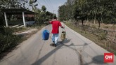 Bermodalkan dua jeriken, warga Desa Ridogalih berjalan menuju rumah usai mengambil air bersih gratis. (CNNIndonesia/Safir Makki)