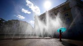 Di Vienna, Austria, seorang gadis berpayung biru berdiri di bawah air mancur pada hari yang diterpa gelombang panas. (Reuters/Lisi Niesner)