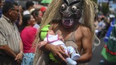 Seorang yang bersuka ria dengan topeng karakter mitologis dan menggendong bayi ikut serta dalam parade yang menandai dimulainya festival Divino Salvador del Mundo. (Photo by Oscar Rivera / AFP)
