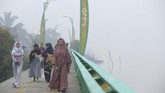 Umat Muslim yang akan menunaikan ibadah Salat Idul Adha berjalan di tepian Sungai Kapuas yang diselimuti kabut asap di Pontianak, Kalimantan Barat, 11 Agustus 2019. (ANTARA FOTO/Jessica Helena Wuysang)