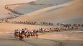 Sekelompok turis tampak menunggangi unta di gurun Dunhuang, China, di barat laut Provinsi Gansu. (STR/AFP)