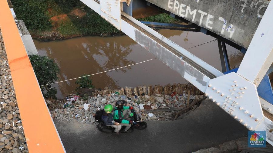 Sebagian jalan sudah tergerus oleh air kali dan hanya di tahan oleh beberapa kayu atau balok di sekitar.