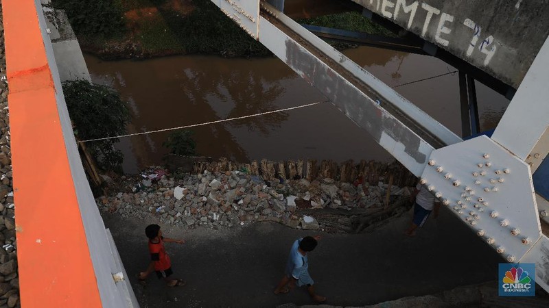 Sebagian jalan sudah tergerus oleh air kali dan hanya di tahan oleh beberapa kayu atau balok di sekitar.