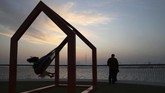 Seorang gadis bermain ayunan sementara matahari terbenam di belakang garis cakrawala dan gedung tertinggi di dunia, Burj Khalifa, terlihat di kejauhan. (AP Photo/Kamran Jebreili)