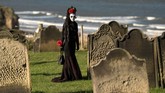 Seorang peserta pesta kostum berjalan di antara batu nisan di pemakaman gereja St Mary, dalam festival 'Whitby Goth Weekend', di Whitby, sebelah utara Inggris. (Photo by OLI SCARFF / AFP)