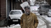 Seorang pria Kashmir menutupi kepalanya dengan kantong plastik saat salju turun di Srinagar, Kashmir pada Kamis (7/11). (AP Photo/Mukhtar Khan)