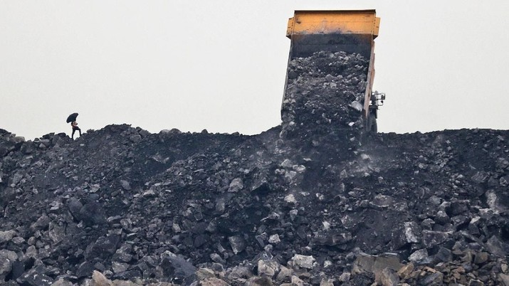 tambang batu bara india berusia seabad In this Oct. 23, 2019, photo, a laborer keeps watch as coal is unloaded from a truck in the village of Rajapur in Jharia, a remote corner of eastern Jharkhand state, India. The fires started in coal pits in eastern India in 1916. More than a century later, they are still spewing flames and clouds of poisonous fumes into the air, forcing residents to brave sizzling temperatures, deadly sinkholes and toxic gases. (AP Photo/Aijaz Rahi)