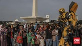 Anak-anak kecil mengamati Transformer berukuran besar yang berjalan melewati mereka di Lapangan Silang Monas, Jakarta Pusat, Minggu (17/11). (CNN Indonesia/Bisma Septalisma)