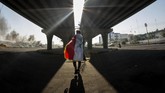 Di kota Basra, seorang demonstran Iraq membungkus dirinya sendiri dengan bendera nasional dan berjalan di bawah suatu jembatan. Ia diselimuti asap dari ban yang dibakar pada suatu aksi memprotes pemerintah. (Photo by Hussein FALEH / AFP)
