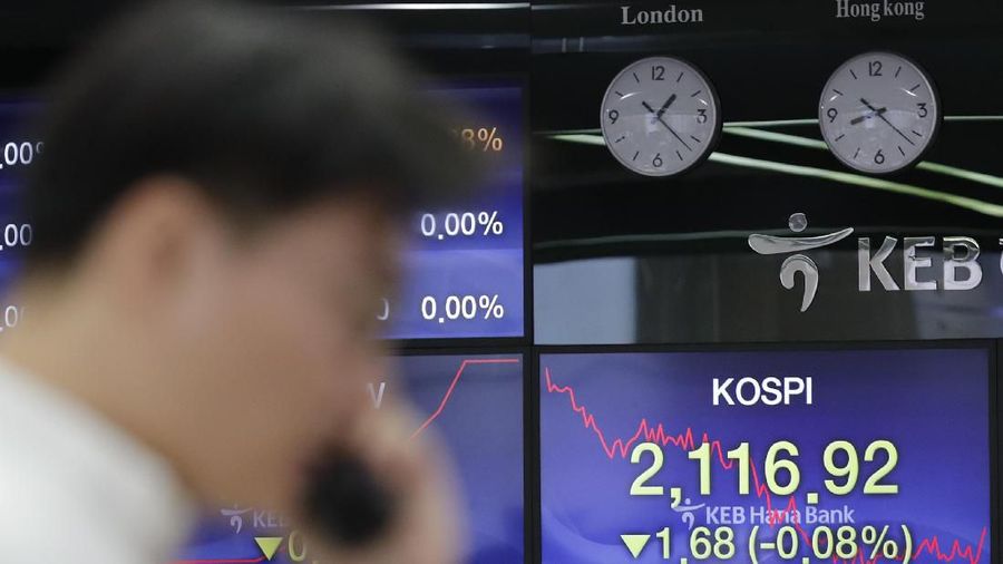 A currency trader walks by the screens showing the Korea Composite Stock Price Index (KOSPI), left, and the foreign exchange rate between U.S. dollar and South Korean won at the foreign exchange dealing room in Seoul, South Korea, Tuesday, Dec. 10, 2019. Asian stock markets have fallen as investors look ahead to interest rate decisions by U.S. and European central bankers and possible American tariff hike on Chinese imports.  (AP Photo/Lee Jin-man)