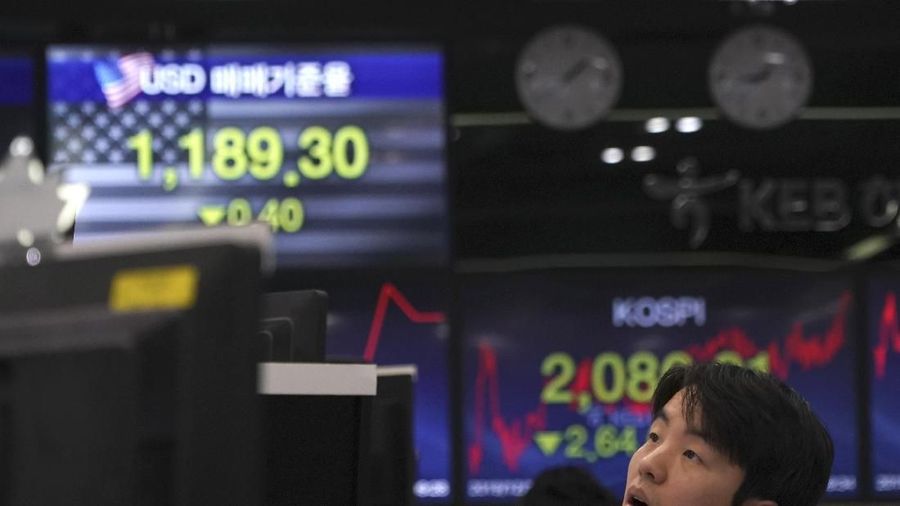 A currency trader walks by the screens showing the Korea Composite Stock Price Index (KOSPI), left, and the foreign exchange rate between U.S. dollar and South Korean won at the foreign exchange dealing room in Seoul, South Korea, Tuesday, Dec. 10, 2019. Asian stock markets have fallen as investors look ahead to interest rate decisions by U.S. and European central bankers and possible American tariff hike on Chinese imports. (AP Photo/Lee Jin-man)