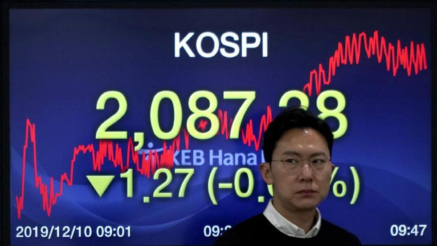 A currency trader walks by the screens showing the Korea Composite Stock Price Index (KOSPI), left, and the foreign exchange rate between U.S. dollar and South Korean won at the foreign exchange dealing room in Seoul, South Korea, Tuesday, Dec. 10, 2019. Asian stock markets have fallen as investors look ahead to interest rate decisions by U.S. and European central bankers and possible American tariff hike on Chinese imports. (AP Photo/Lee Jin-man)