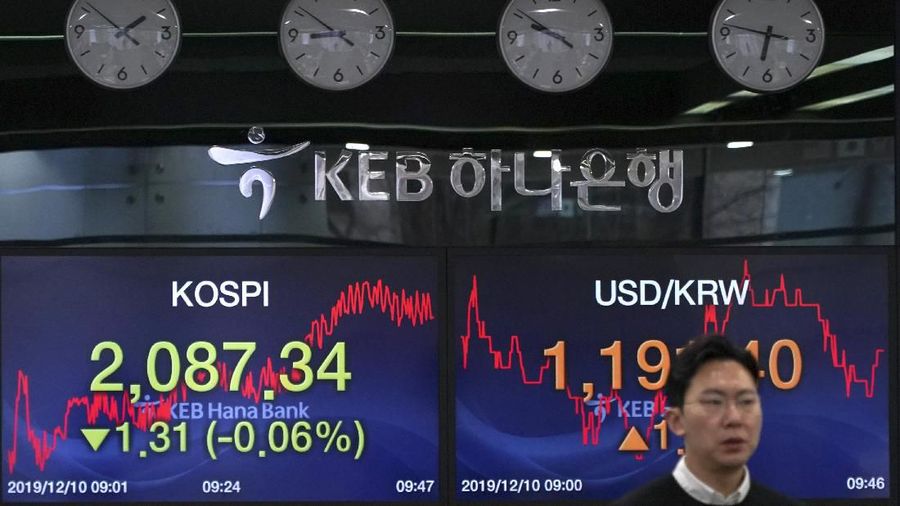A currency trader walks by the screens showing the Korea Composite Stock Price Index (KOSPI), left, and the foreign exchange rate between U.S. dollar and South Korean won at the foreign exchange dealing room in Seoul, South Korea, Tuesday, Dec. 10, 2019. Asian stock markets have fallen as investors look ahead to interest rate decisions by U.S. and European central bankers and possible American tariff hike on Chinese imports.  (AP Photo/Lee Jin-man)
