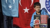 Seorang bocah pendukung muslim Uighur berdiri di depan bendera Turki dan Turkestan Timur sambil memegang poster dukungan untuk Mesut Ozil. (Ozan KOSE / AFP)