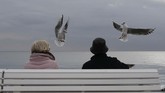 Dua orang duduk di bangku taman melihat burung camar di Promenade des Anglais di kota Nice, Perancis. (Photo by VALERY HACHE / AFP)