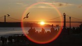 Orang-orang berdiri di pinggiran sungai Tagus sambil menyaksikan matahari yang tenggelam di Lisbon, Portugal. (AP Photo/Armando Franca)