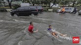 Anak-anak bermain air di tengah genangan di jalan raya yang masih dilalui kendaraan bermotor. (CNN Indonesia/ Adhi Wicaksono)