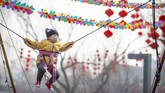Seorang anak mengenakan topeng wajah bermain ayunan di dekat dekorasi sebuah kuil tempat perayaan Tahun Baru Imlek yang dibatalkan di Longtan Park di Beijing pada Sabtu (25/1). (AP Photo/Mark Schiefelbein)
